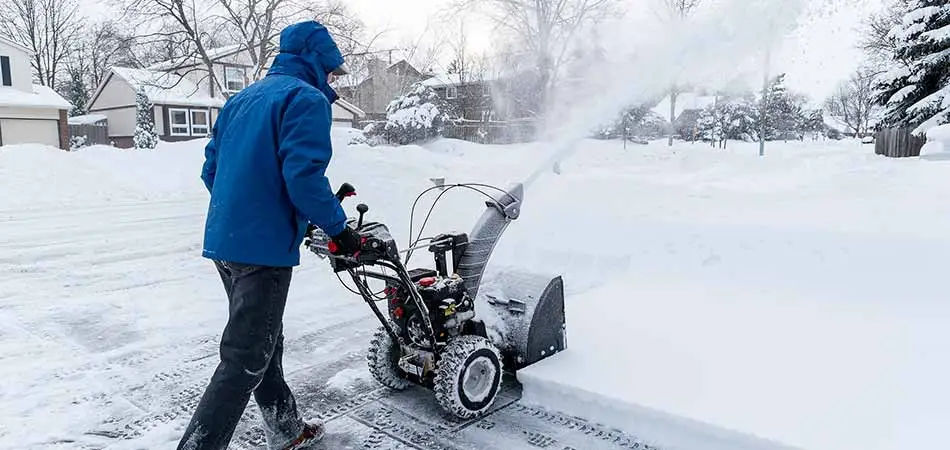 Landscape worker using a snow blower to remove snow from a St. Cloud, MN property.