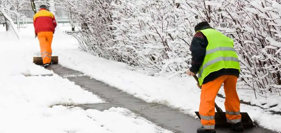 Two experienced team members clearing the snow from a sidewalk in front of a %%targetarea2% area customer.